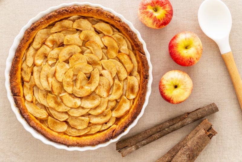 A fresh apple tart on a table next to three apples and a spoon