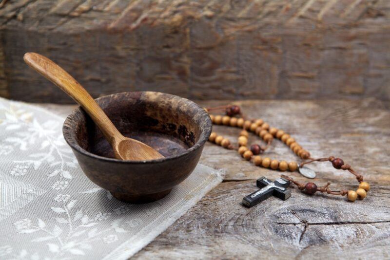 An empty wooden bowl with a spoon, next to some prayer beads