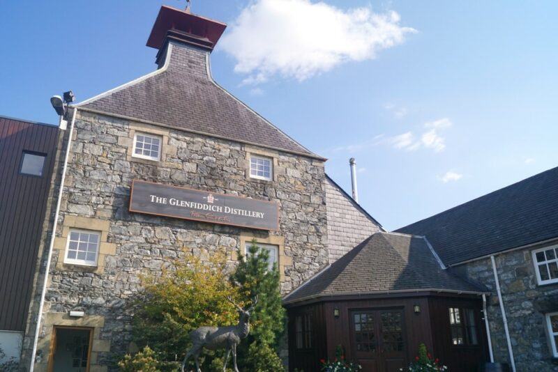 An outdoors image of the Glenfiddich distillery on a sunny day with a few white clouds in the sky