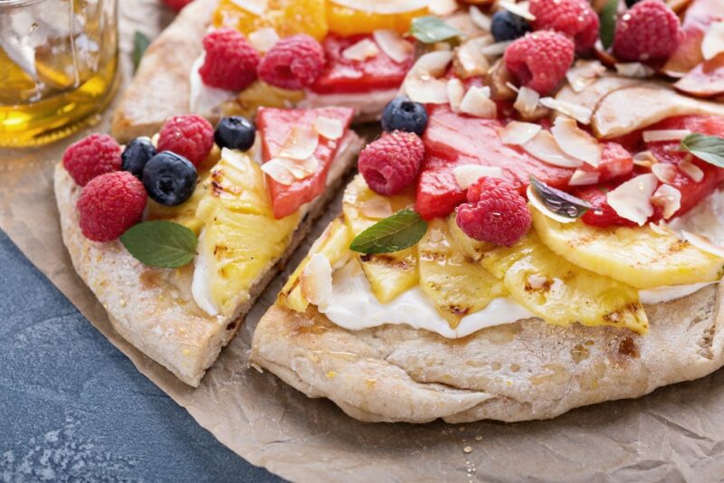 A wooden tray with a dessert pizza that uses a cream cheese topping with honey and plenty of fresh fruit