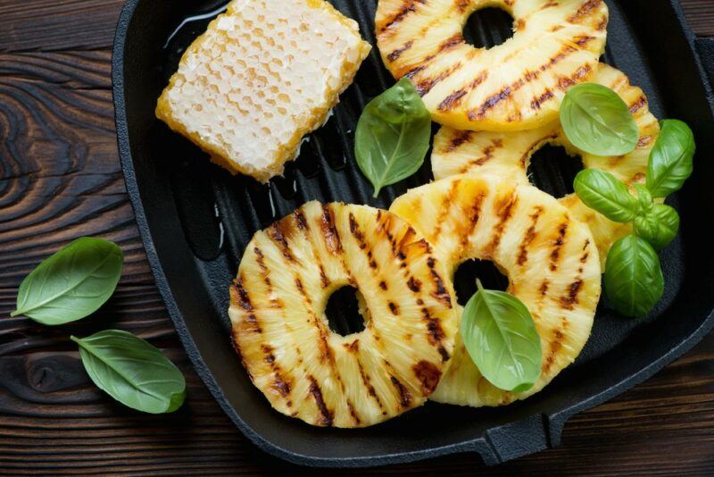 A black frypan with grilled pineapple slices and some leaves