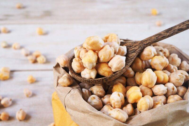 An open bag containing chickpeas, some of which are being scooped out with a spoon