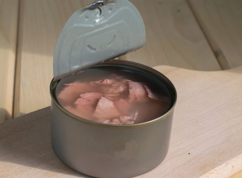 A metal tin of tuna with juice on a wooden deck