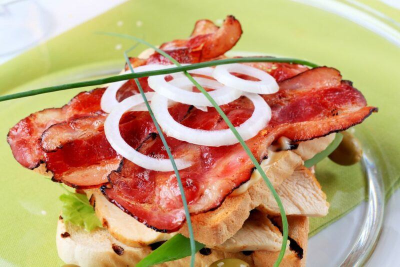 A lime green plate with an open face sandwich with turkey bacon, raw onion slices, and chives