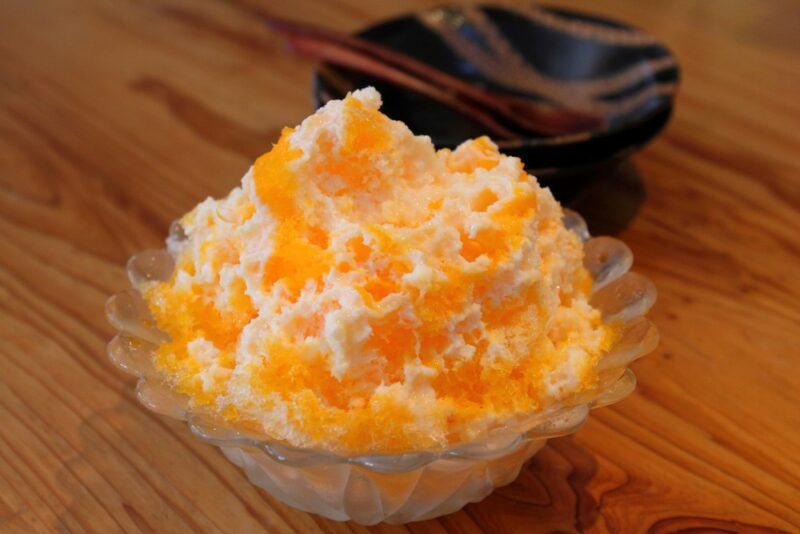 A glass container with an orange creamsicle snow cone