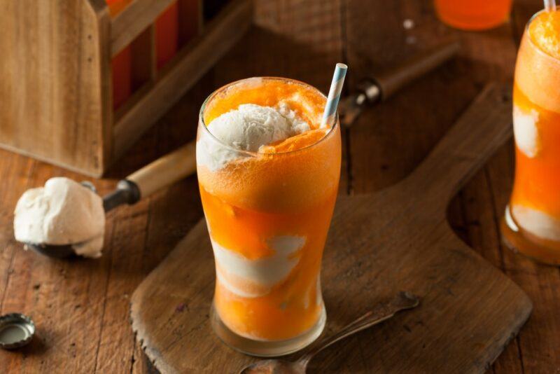 A tall glass containing an orange dreamsicle moonshine cocktail with ice cream and a straw