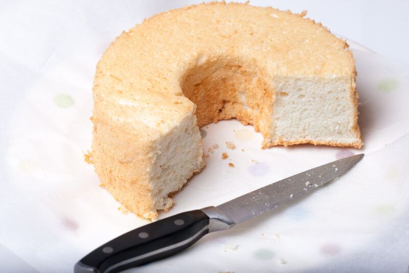 a closeup image of a half a pan of Angel cake with a knife with black handle beside it