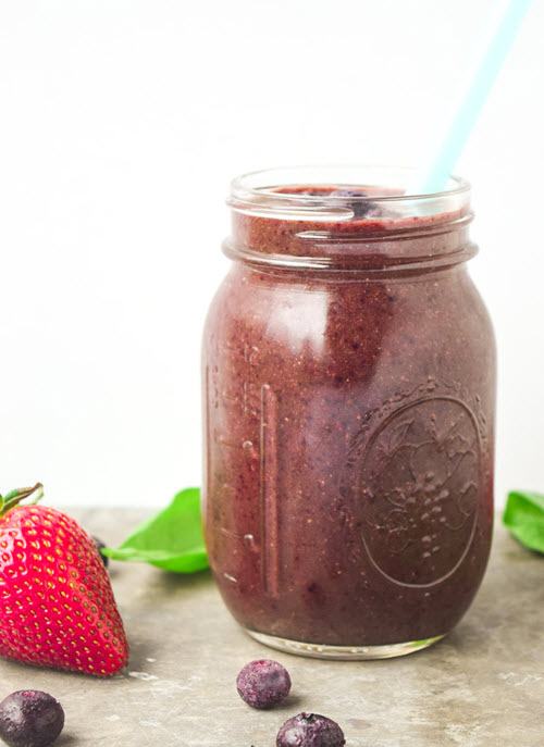 A purple smoothie in a mason jar with a straw