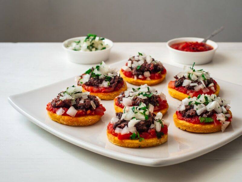 Small appetizers made using chopped raw onion and served on a square white plate