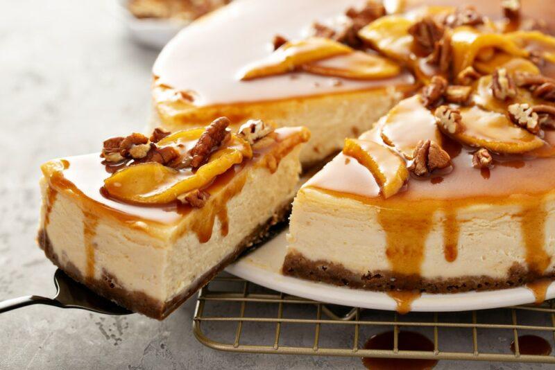 A cheesecake on a white plate with caramel topping, apples, and pecans