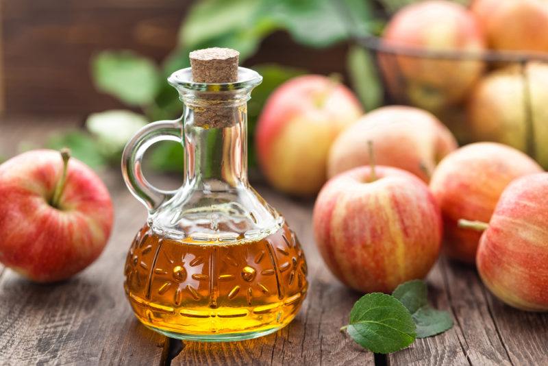 A jar of apple cider with apples on the table