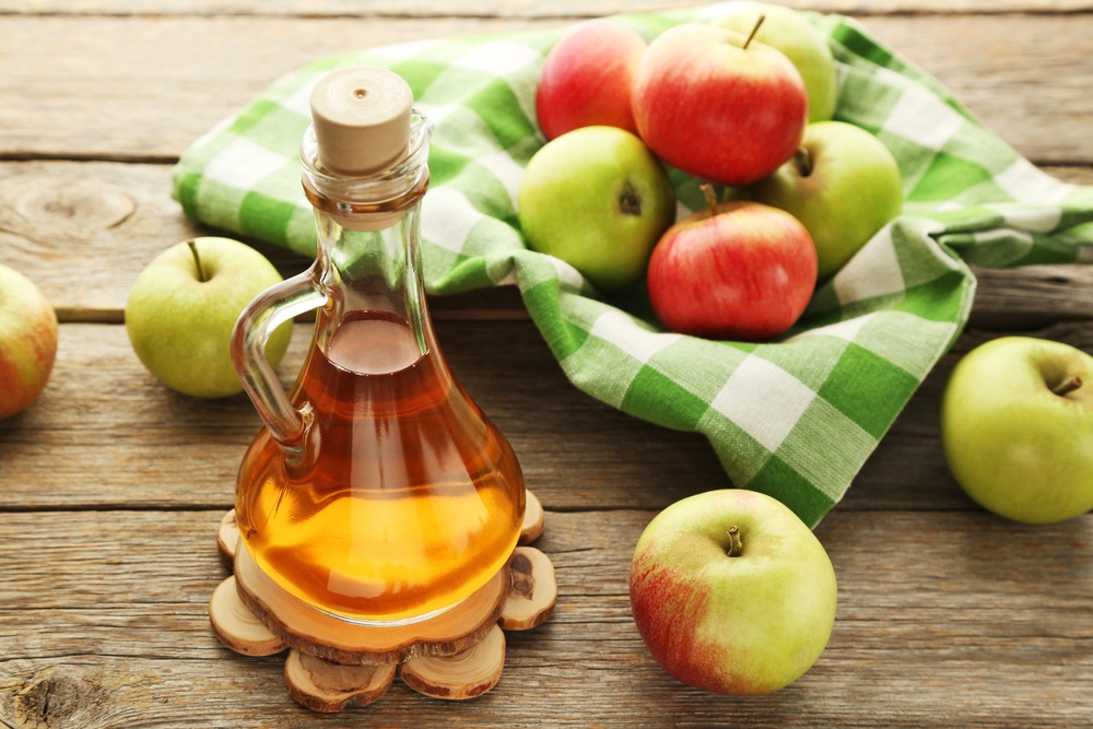 A container of apple cider vinegar with a basket of apples