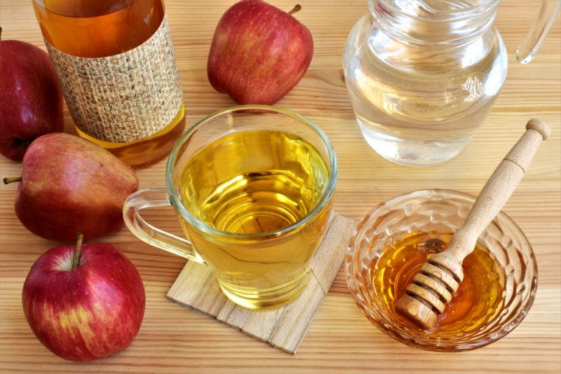 A glass mug of apple cider vinegar, water and honey, with apples and honey scattered around