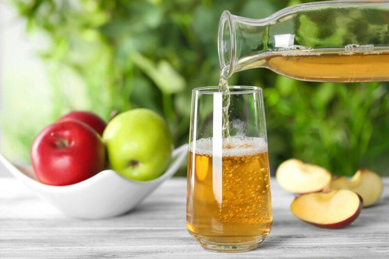 A glass of apple juice being poured from a jug, next to a green and red apple