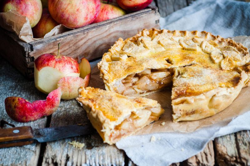 A deep dish apple pie next to a crate of apples