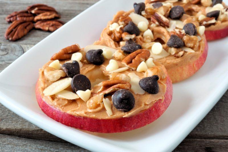 Three rounds of sliced apple with peanut butter, chocolate, and nuts