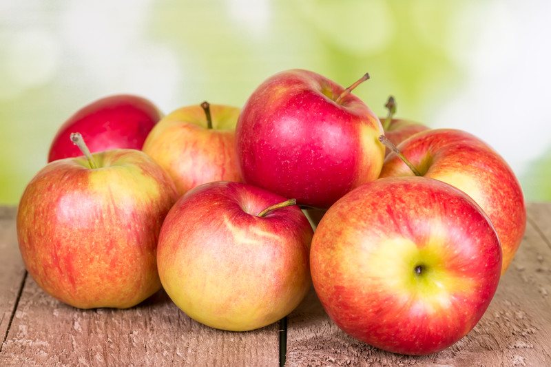 Several red apples rest on a wooden surface.