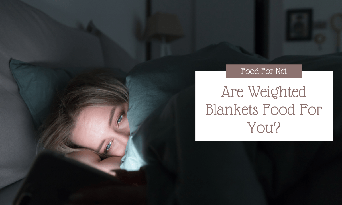 A young woman snuggled into bed looking at her phone, highlighting the idea of whether weighted blankets are good for you
