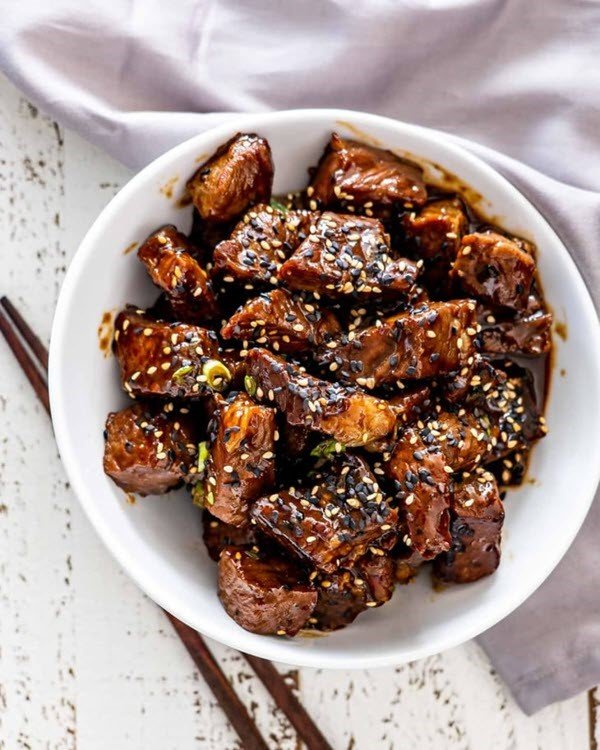 A white plate with Asian steak bites and chopsticks