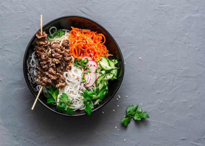 A black bowl that contains various asian ingredients, including beef