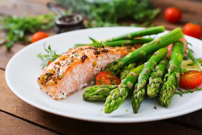 A white plate with a dinner of cooked salmon and asparagus