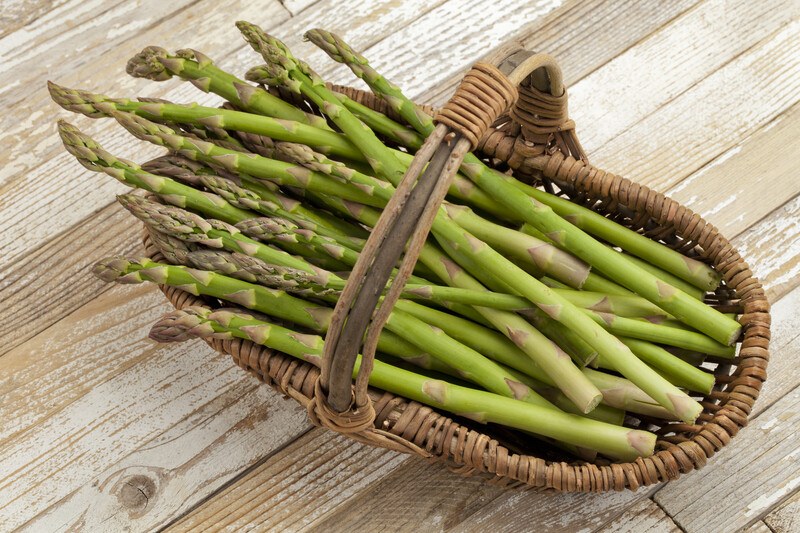 Several spears of asparagus like in a brown wicker basket on a wooden background.