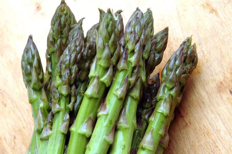 This photo shows a bunch of green asparagus spears on a wooden table.