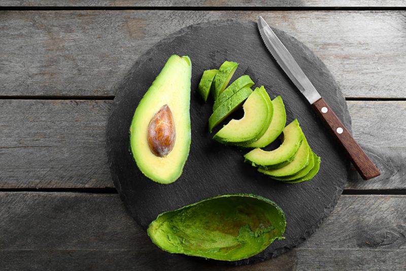 Half of an avocado and a sliced avocado on a black plate