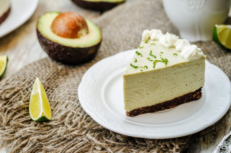 An avocado cheesecake on a white plate with avocado next to it