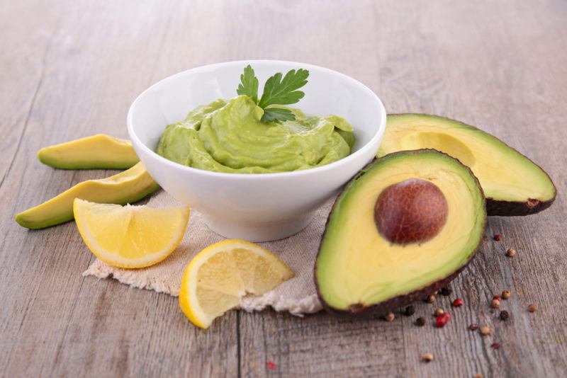 A bowl of avocado dip next to avocados and lemons