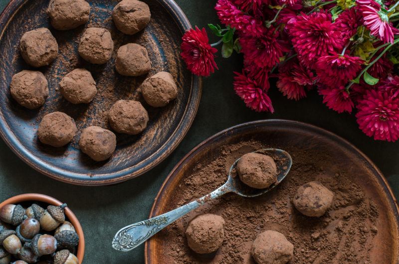 Chocolate avocado fat bombs being dipped in cocoa