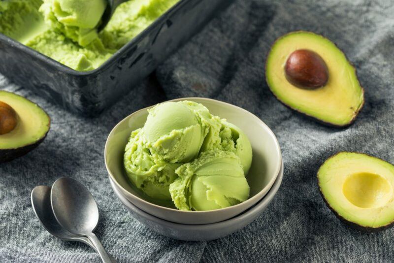 A small bowl of avocado ice cream, next to some avocado halves