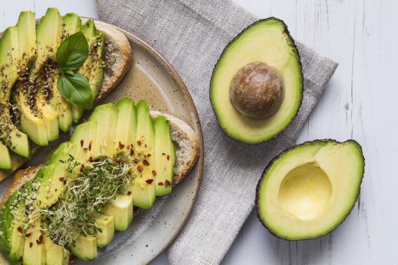 An avocado that has been cut in half, next to two pieces of mushroom toast