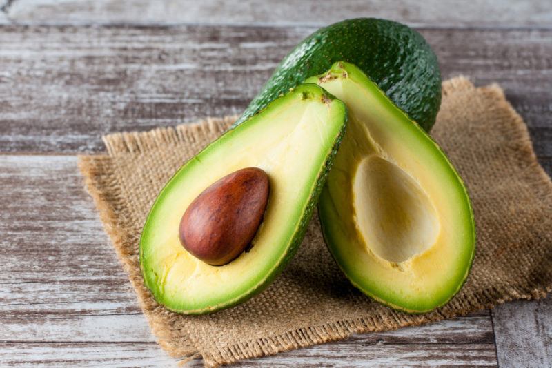 A whole avocado and one that has been sliced open on a table