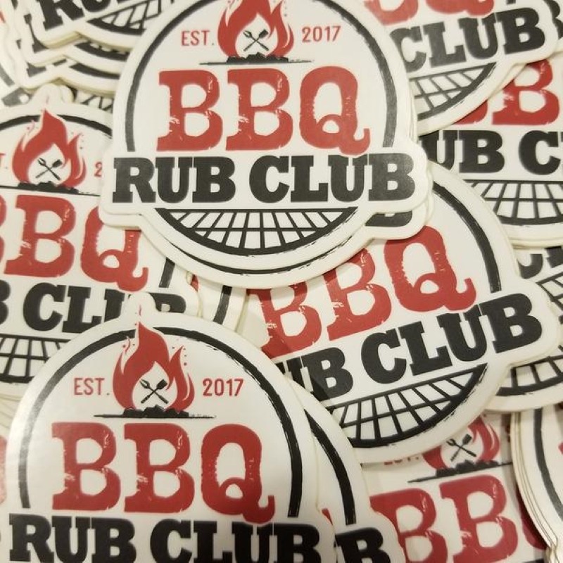 A pile of stickers - The stickers are mostly round, with a white background, at the top in red it says est. 2017 with a bonfire in between the year and est.  Then in large Red Font it says BBQ, below that in Black font Rub Club and at the bottom a grill grate.