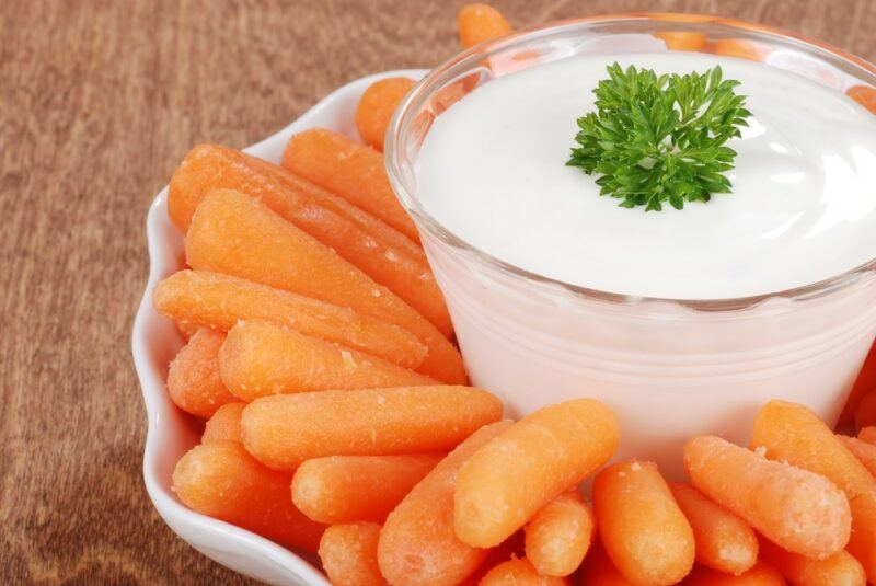 A white scalloped dish filled with fresh baby carrots and a large bowl of dip