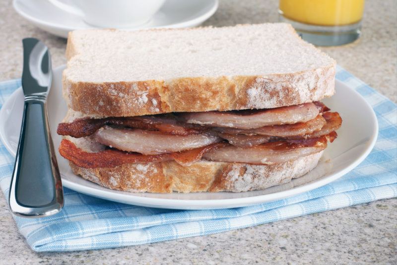 A bacon sandwich with white bread on a white plate