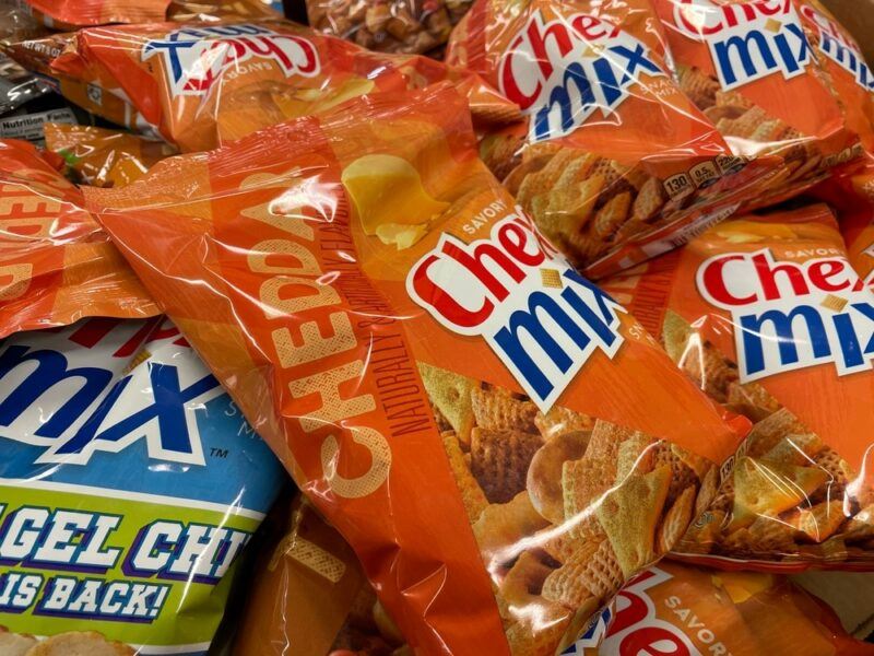 A pile of Chex Mix bags. Most are orange, but one is blue and green instead.