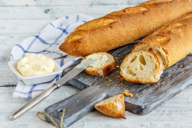 Two baguettes, one that has been sliced, along with butter and a cloth