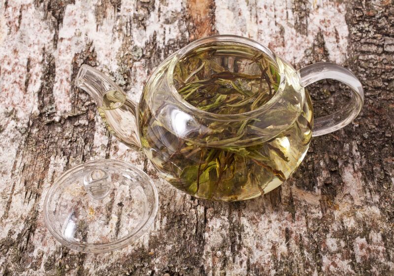 a rustic wooden surface with a clear tea pot with Bai Mudan tea