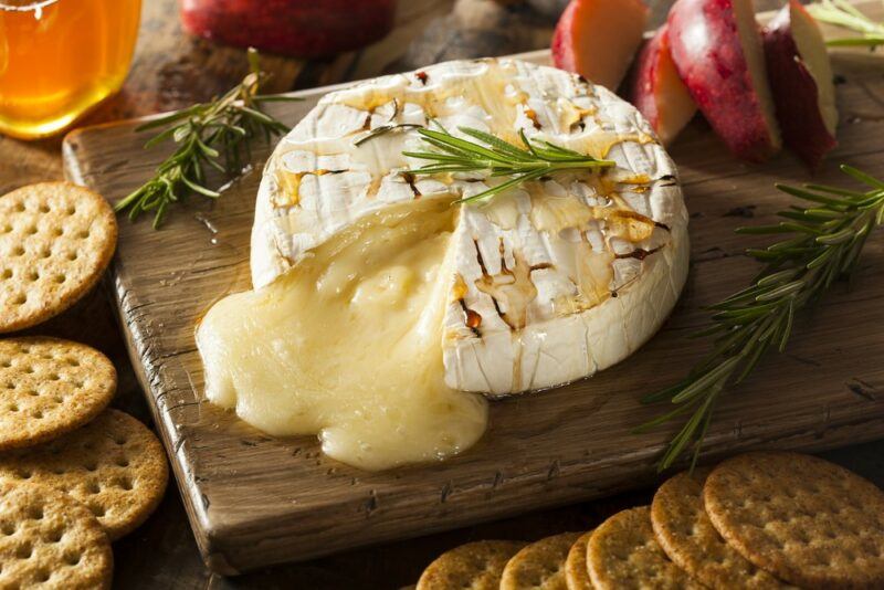 A wooden board with a wheel of baked brie that is melting