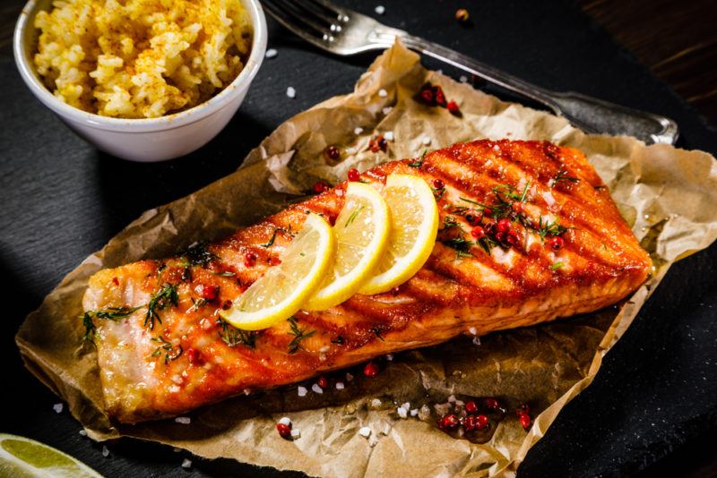 Baked salmon with lemon on baking paper with a small bowl of rice