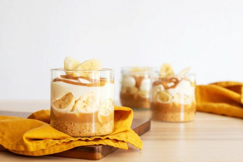 Three glasses containing a banoffee pie pudding on a wooden table