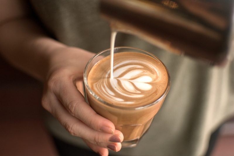 A hand pouring coffee into milk and making coffee art