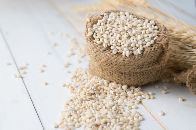 A sack of barley with barley spilling out onto a wooden table