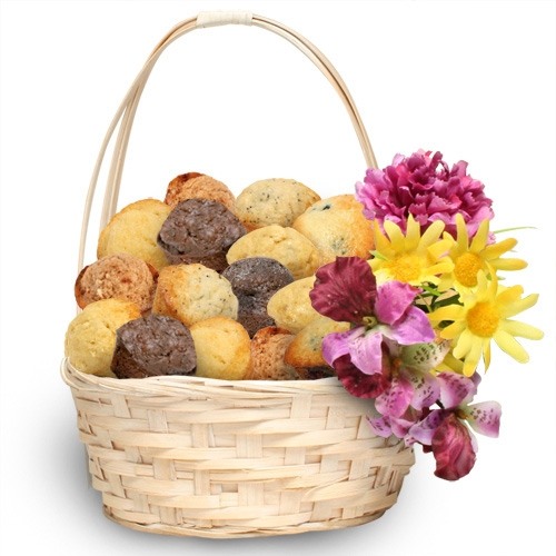 light colored wicker basket with narrow triple hoop handle mounded with an assortment of muffins and on the right side pink and yellow flowers