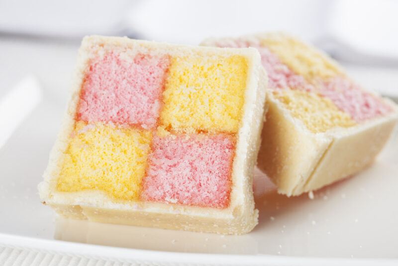 a closeup image of a couple of slices of Battenberg cake on a white ceramic dish