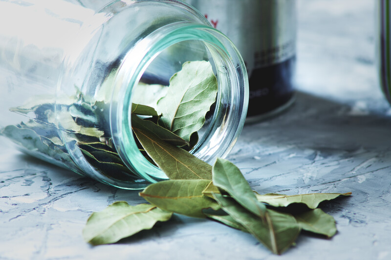 bay leaf pouring out of a small toppled over glass jar on a marble surface