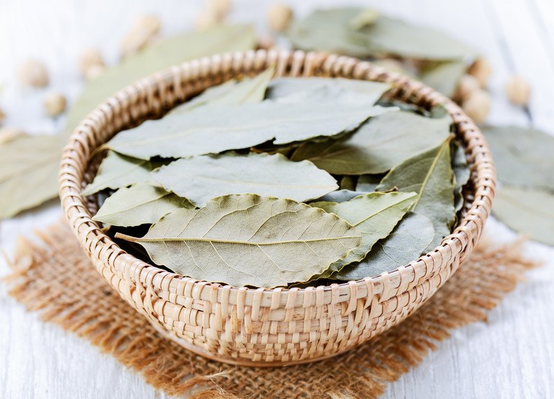 a small rattan bowl full of dried bay leaves resting on a piece of sack cloth, with lose dried bay leaves at the back