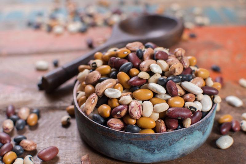 A bowl filled with different beans, next to a metal spoon